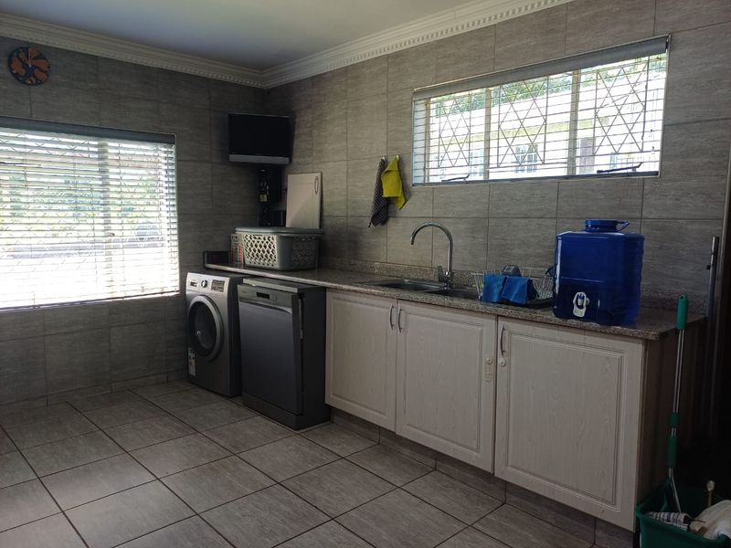 A functional laundry room featuring tiled walls and floors, built-in cabinetry with a stone countertop, and a stainless steel sink.