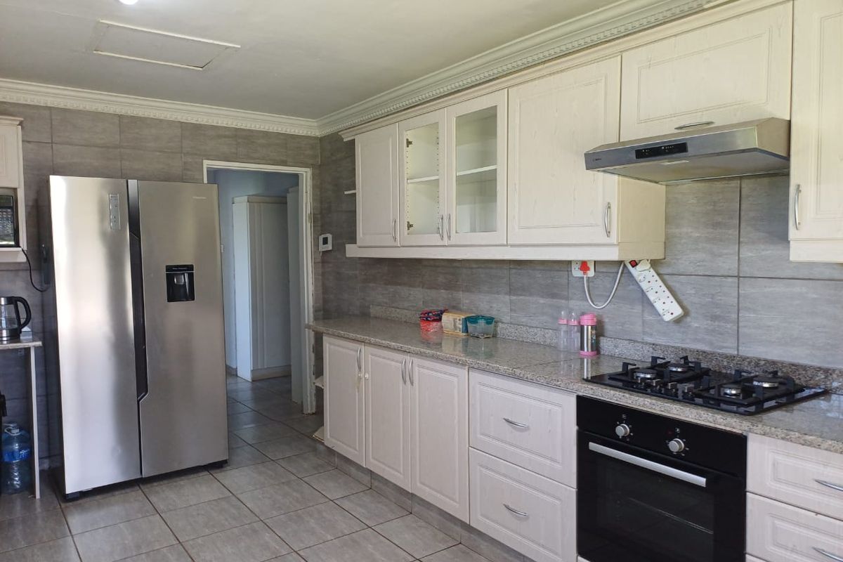 A functional kitchen featuring white cabinetry, granite countertops, a gas hob, built-in oven, and neutral tiled flooring with a tiled backsplash.