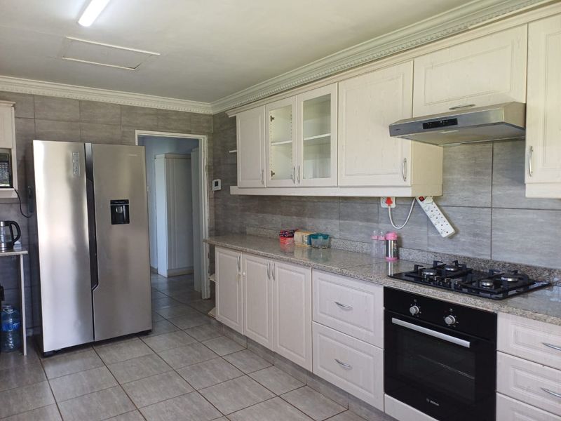 A functional kitchen featuring white cabinetry, granite countertops, a gas hob, built-in oven, and neutral tiled flooring with a tiled backsplash.