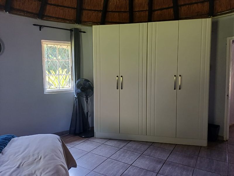 A bedroom featuring a unique thatched ceiling, tiled flooring, and a large built-in wardrobe with white cabinetry.