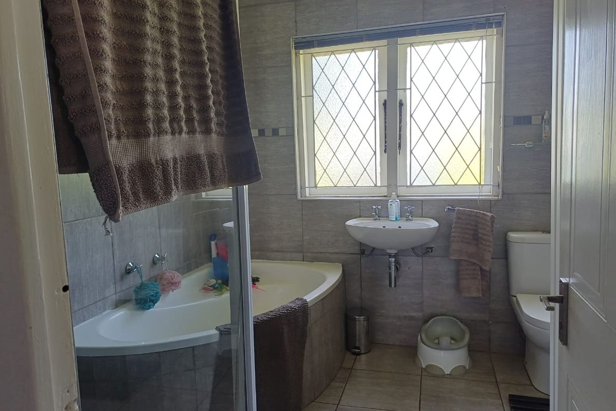 A functional bathroom featuring a built-in bathtub, wall-mounted basin, toilet, and neutral wall and floor tiling with a leaded glass window.