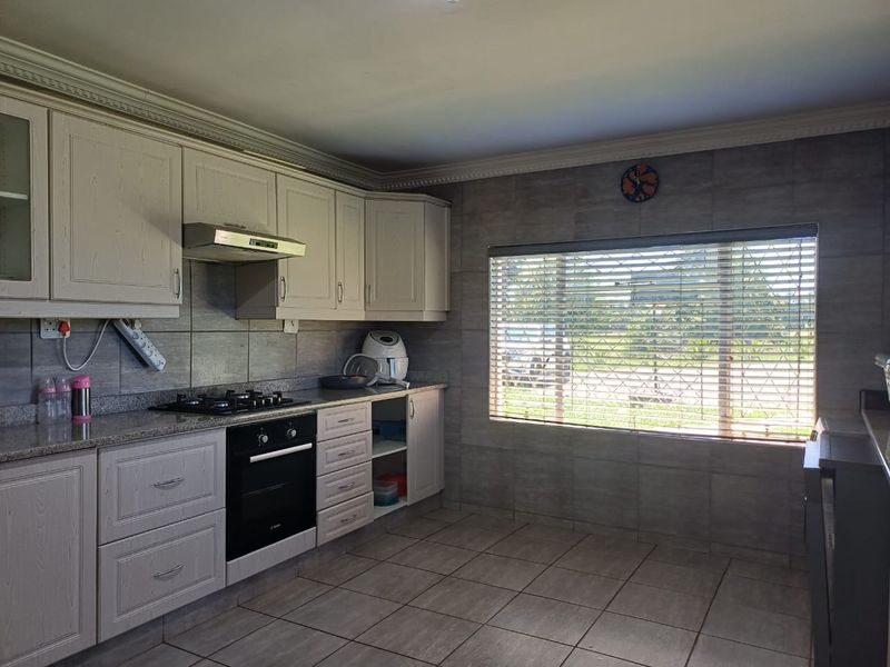A functional kitchen featuring light-toned cabinetry, granite countertops, a built-in gas hob, electric oven, and tiled finishes throughout.