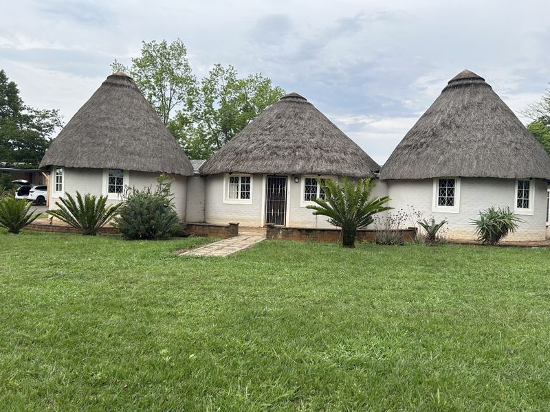 A unique property featuring three interconnected round structures with traditional thatched roofs, lattice windows, and a well-maintained front lawn.