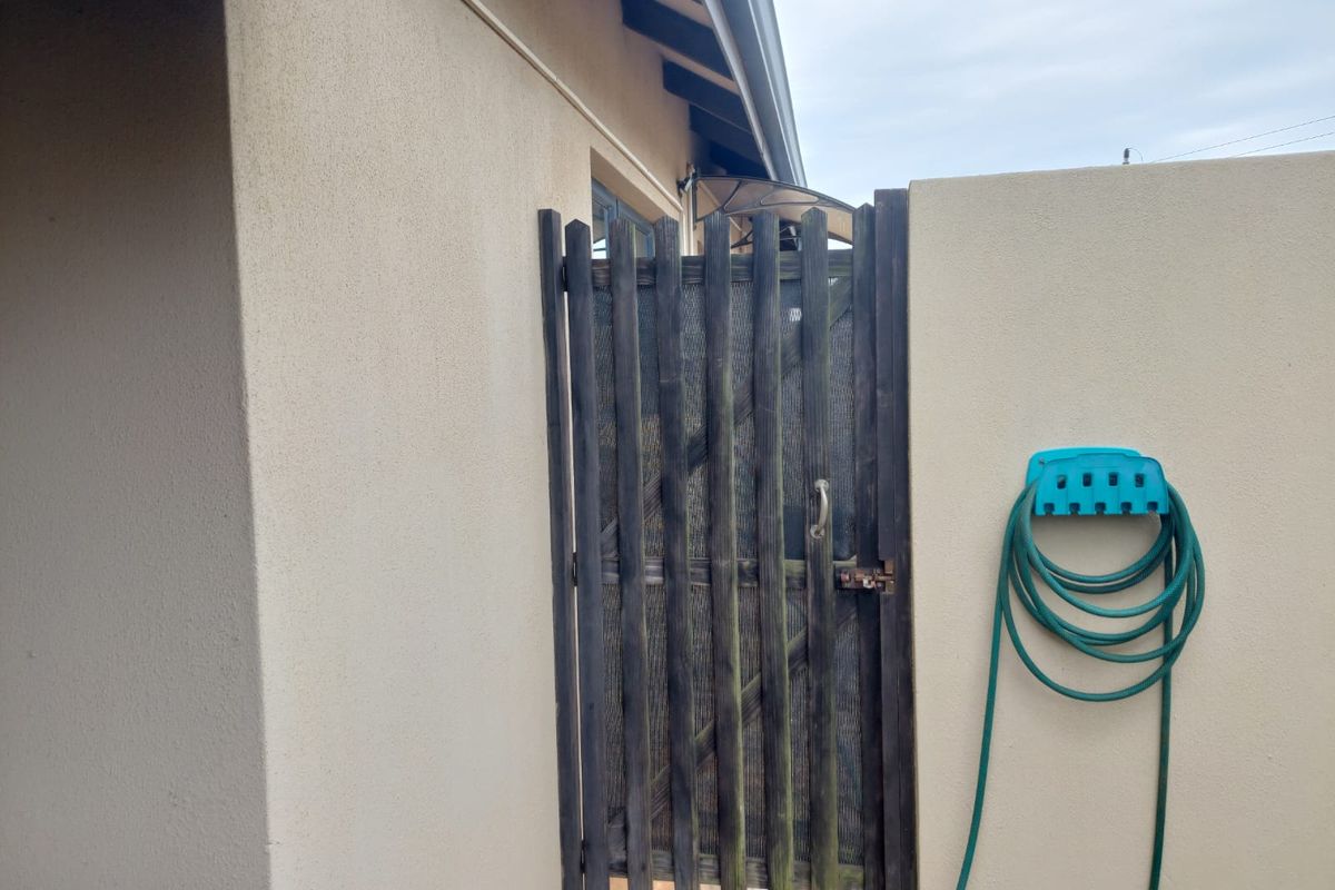 A side access area featuring a timber gate set between a plastered boundary wall and the main house structure.