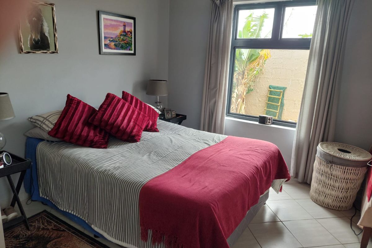 A functional bedroom featuring tiled flooring and an aluminium-framed window overlooking a private outdoor area.