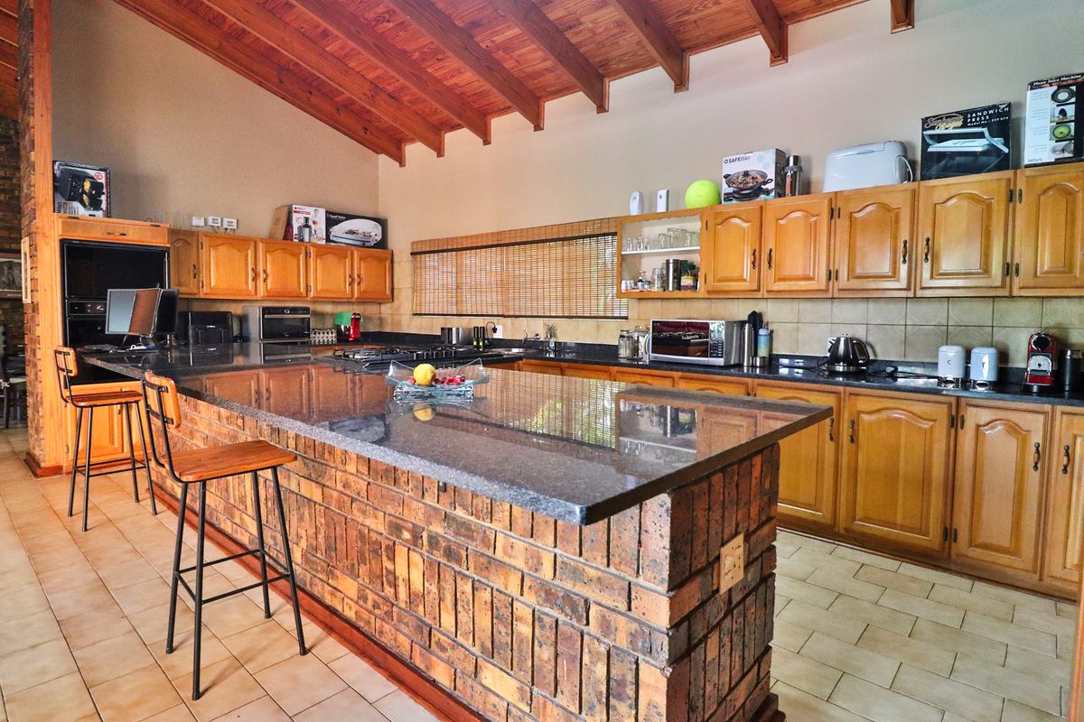 Spacious kitchen featuring a large brick island with granite countertops, exposed timber beam ceilings, and extensive wooden cabinetry.
