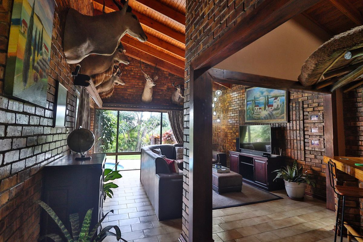 Spacious living area featuring rustic exposed brick walls, high timber-beamed ceilings, and large sliding glass doors providing natural light and garden views.