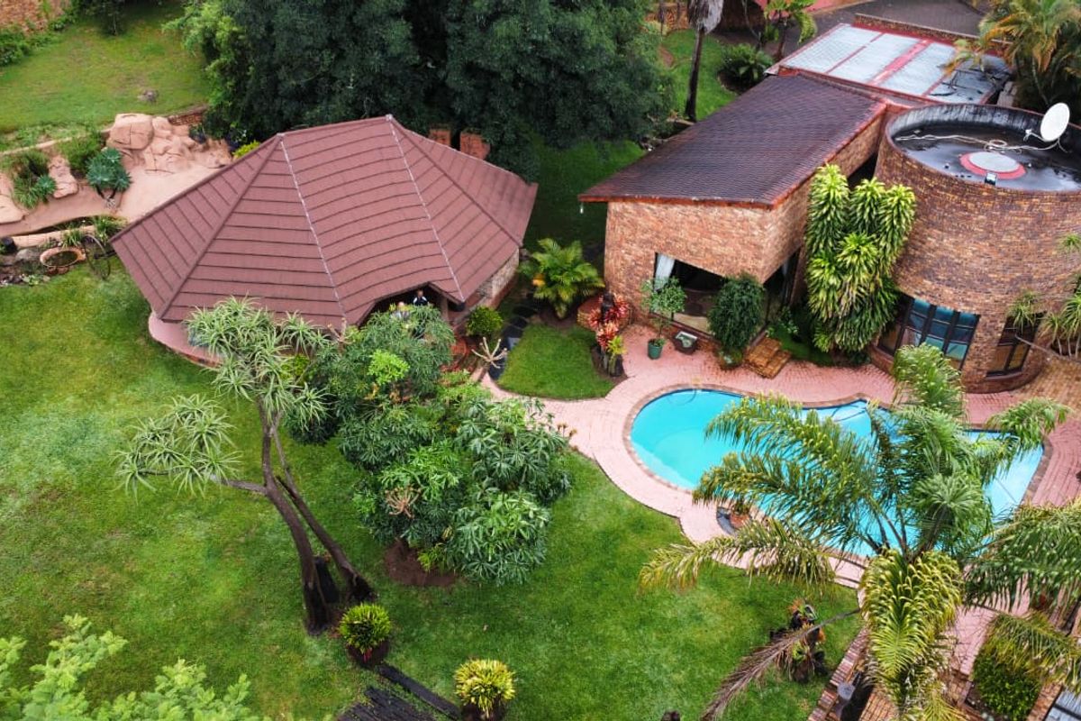 Aerial view of a residential property featuring a swimming pool, landscaped garden, and multiple brick-built structures with tiled roofing.