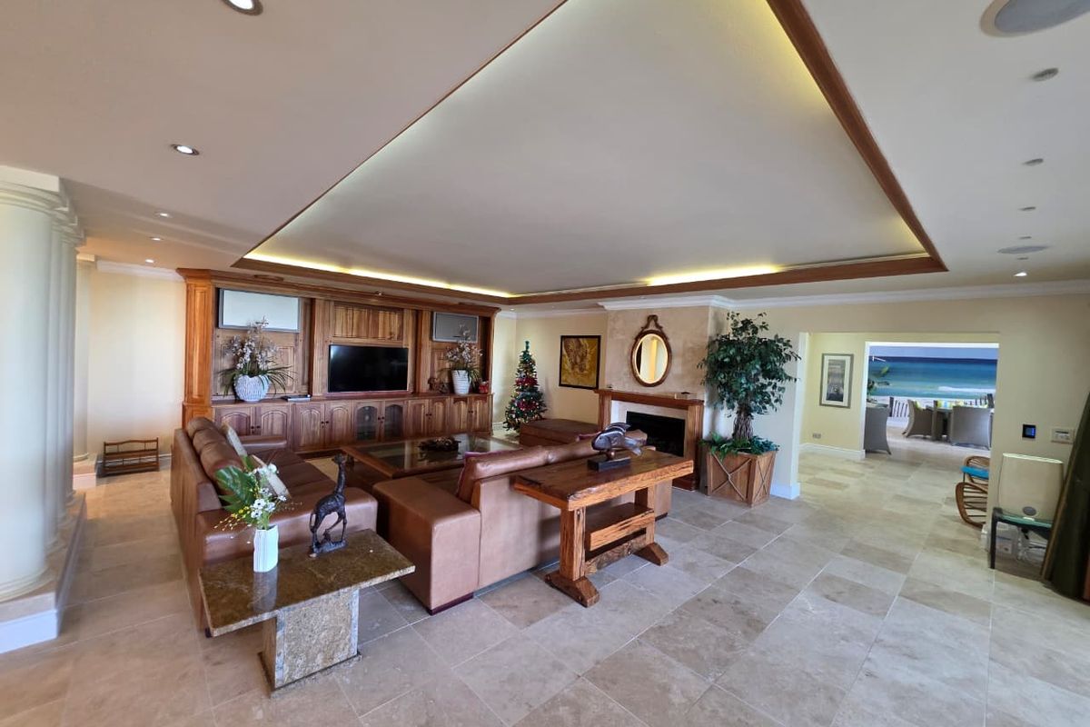 Spacious living room featuring stone tile flooring, custom built-in cabinetry, a fireplace, and elegant cove lighting with recessed spotlights.