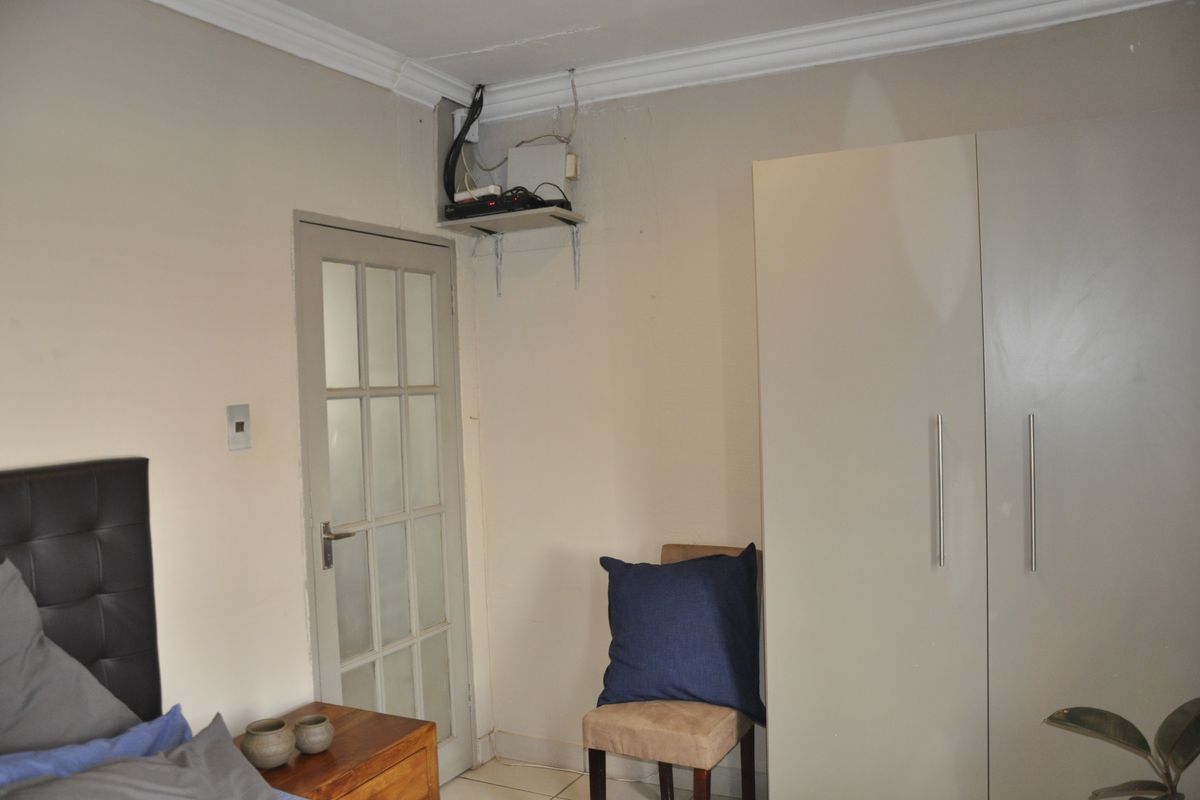 Bedroom featuring a built-in wardrobe, crown molding, and a glass-paneled door, with visible wall imperfections and exposed wiring requiring attention.