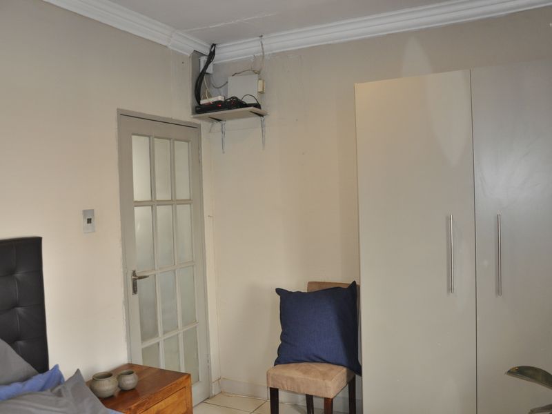 Bedroom featuring a built-in wardrobe, crown molding, and a glass-paneled door, with visible wall imperfections and exposed wiring requiring attention.