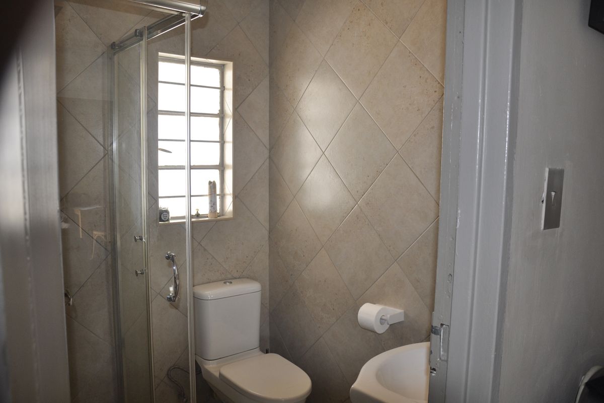A compact bathroom featuring a glass shower enclosure, a standard toilet, and a wall-mounted basin with neutral diamond-patterned wall tiles.