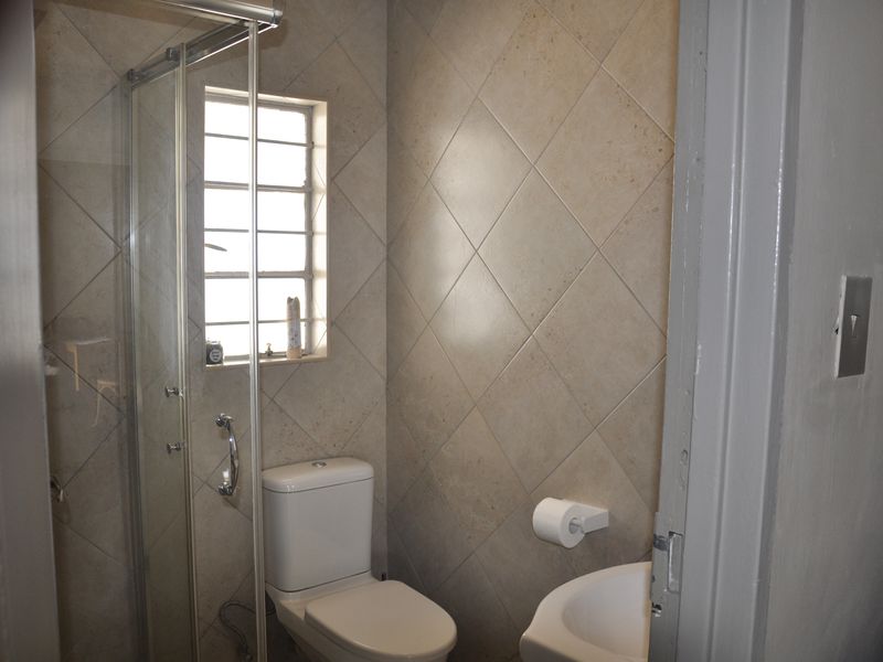 A compact bathroom featuring a glass shower enclosure, a standard toilet, and a wall-mounted basin with neutral diamond-patterned wall tiles.
