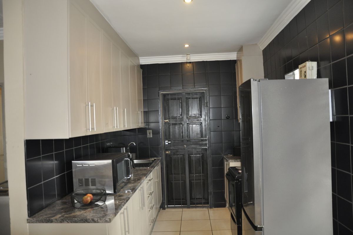 A functional kitchen featuring light-toned cabinetry, dark tiled walls, and stone-look countertops, providing a practical workspace with direct access to an exterior security door.