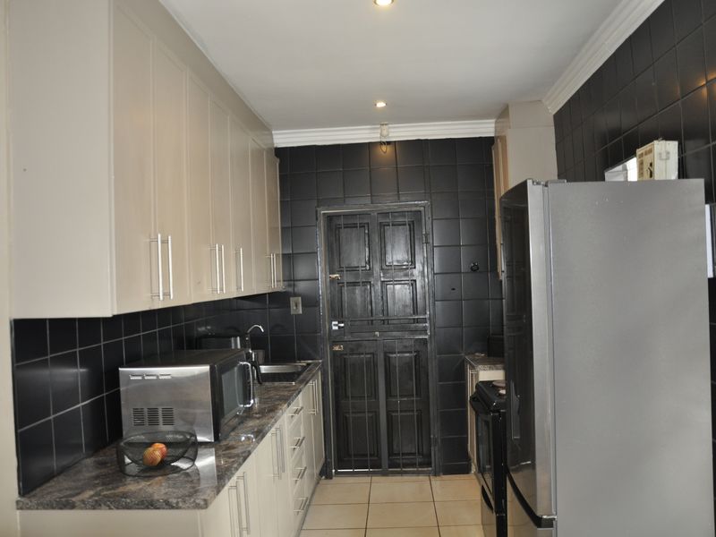 A functional kitchen featuring light-toned cabinetry, dark tiled walls, and stone-look countertops, providing a practical workspace with direct access to an exterior security door.