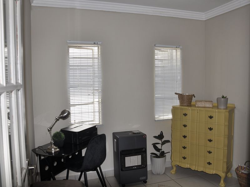 A functional office space featuring tiled flooring, crown molding, and dual windows with fitted venetian blinds.