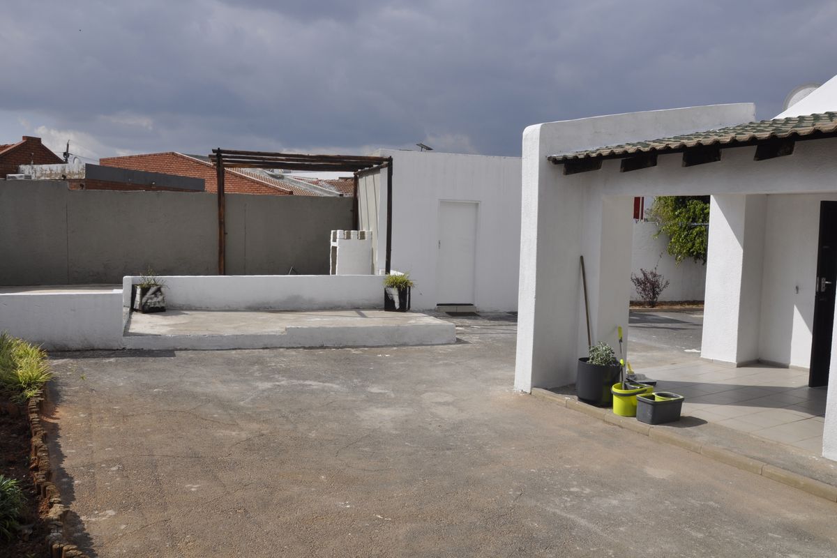 Rear exterior area featuring a paved courtyard, a raised concrete platform with a timber pergola frame, and a covered patio section.