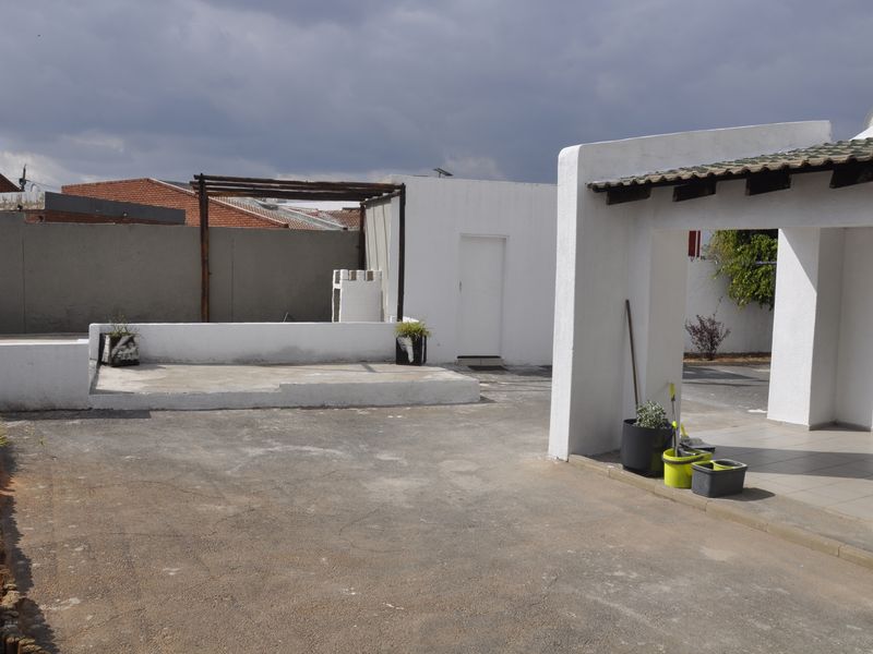 Rear exterior area featuring a paved courtyard, a raised concrete platform with a timber pergola frame, and a covered patio section.