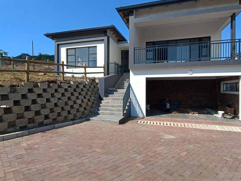 Modern double-story cluster home featuring a paved driveway, retaining wall, concrete staircase, and an integrated garage with an upper balcony.
