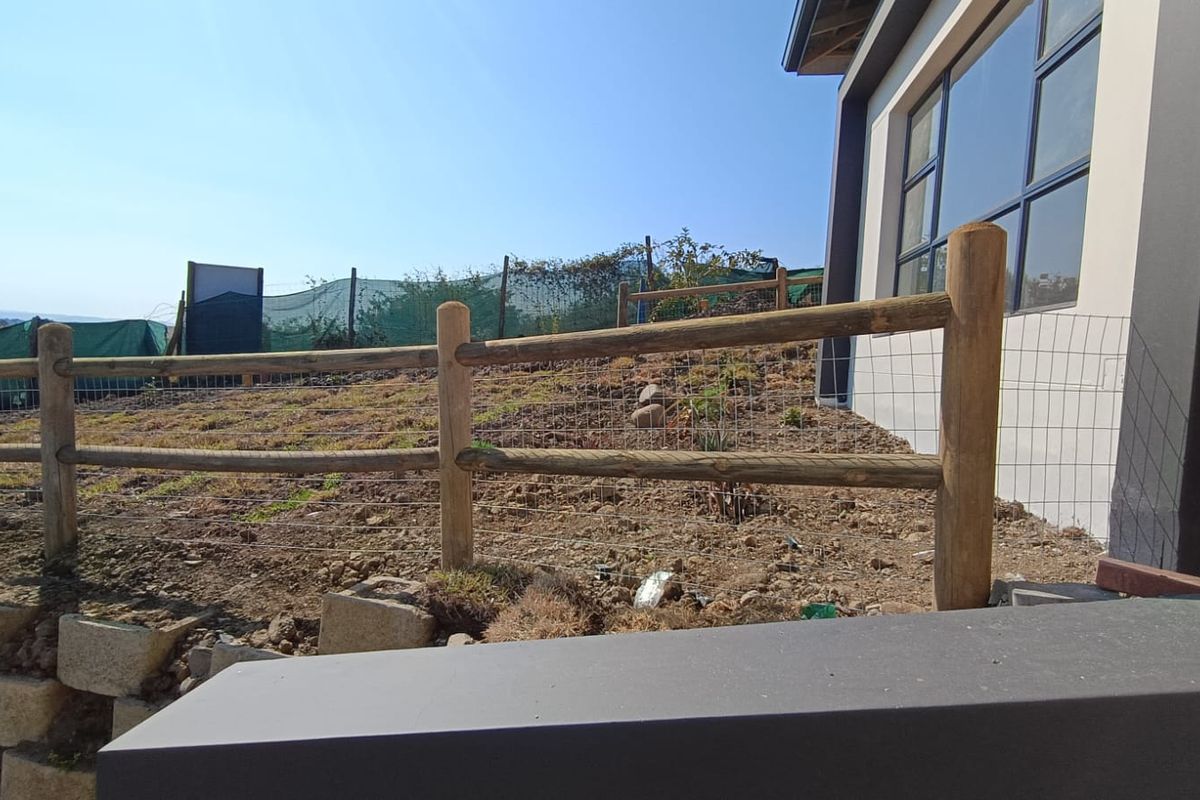 Rear garden area featuring a timber post and wire fence, retaining wall blocks, and views of the adjacent property exterior.
