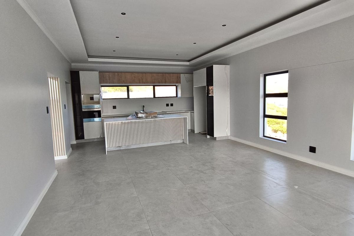 A modern, spacious open-plan living and kitchen area featuring neutral grey tones, tiled flooring, recessed ceiling lights, and a contemporary kitchen island.