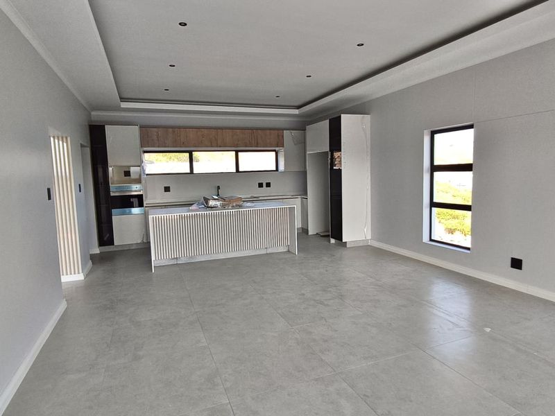 A modern, spacious open-plan living and kitchen area featuring neutral grey tones, tiled flooring, recessed ceiling lights, and a contemporary kitchen island.