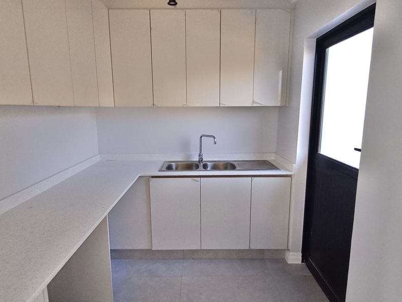 A clean and functional scullery featuring ample built-in cabinetry, a double basin sink with mixer tap, and durable stone countertops.
