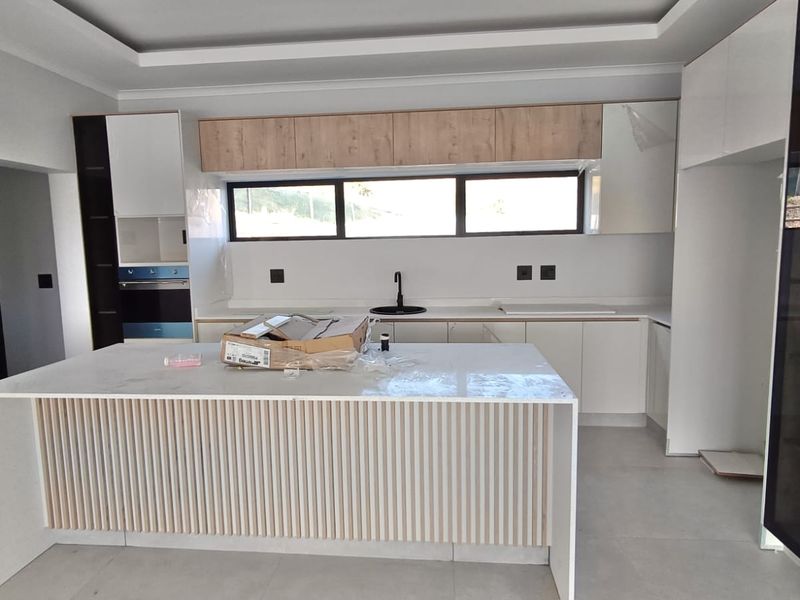 A modern, newly installed kitchen featuring a central island, sleek cabinetry, stone countertops, and a built-in oven in a bright, open-plan space.