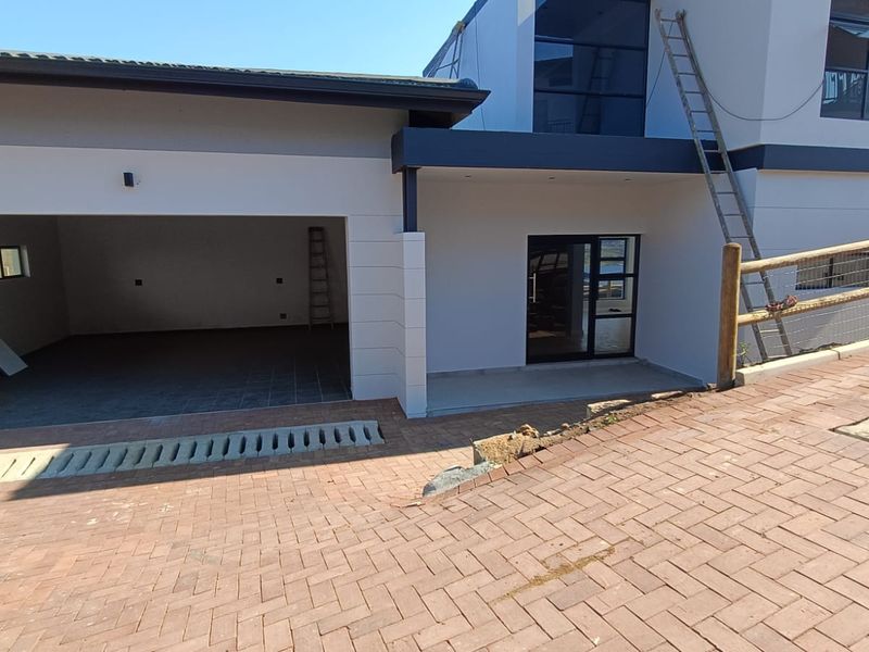 Front exterior view of a modern cluster home featuring a double garage, paved driveway, and contemporary architectural finishes with ongoing site work.