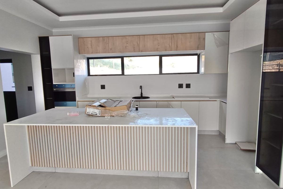 A modern, newly installed kitchen featuring a central island, sleek cabinetry, stone countertops, and a built-in oven in a bright, open-plan space.