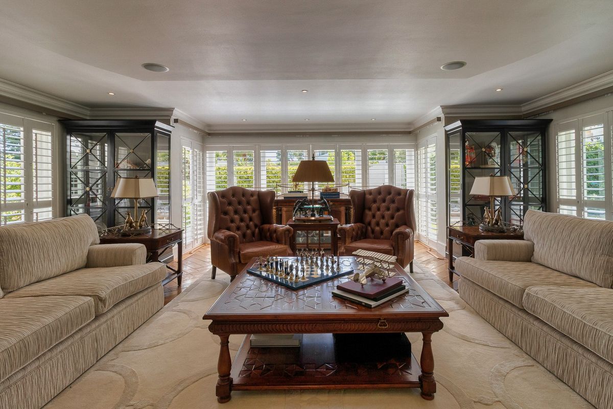 Elegant living room featuring hardwood flooring, built-in display cabinetry, and plantation shutters, creating a sophisticated and well-maintained space.