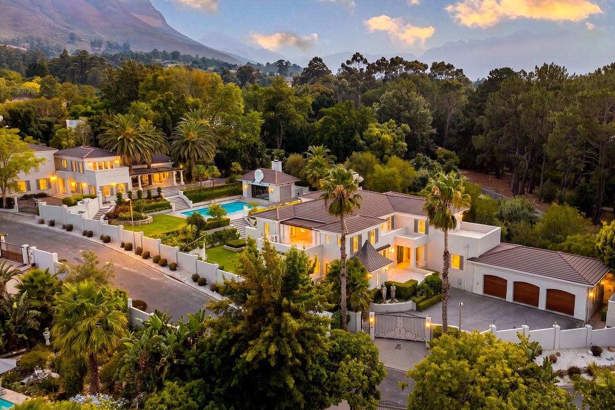 An expansive aerial view of a luxury residential estate featuring multiple buildings, a swimming pool, landscaped gardens, and secure gated access.