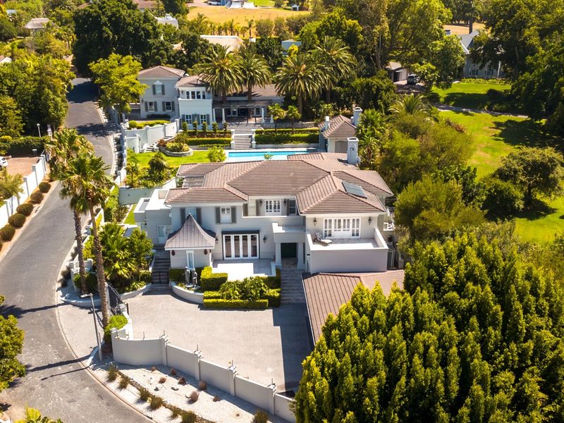 Aerial view of a large, well-maintained residential property featuring a tiled roof, paved driveway, swimming pool, and extensive landscaped gardens in a quiet neighborhood.