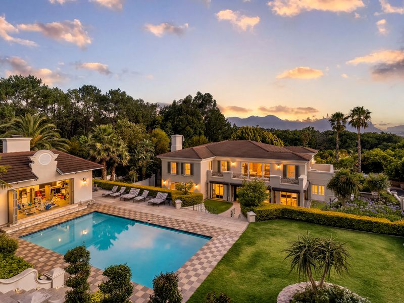 Stunning rear elevation featuring a swimming pool, manicured garden, and spacious balcony, set against a scenic mountain backdrop at sunset.