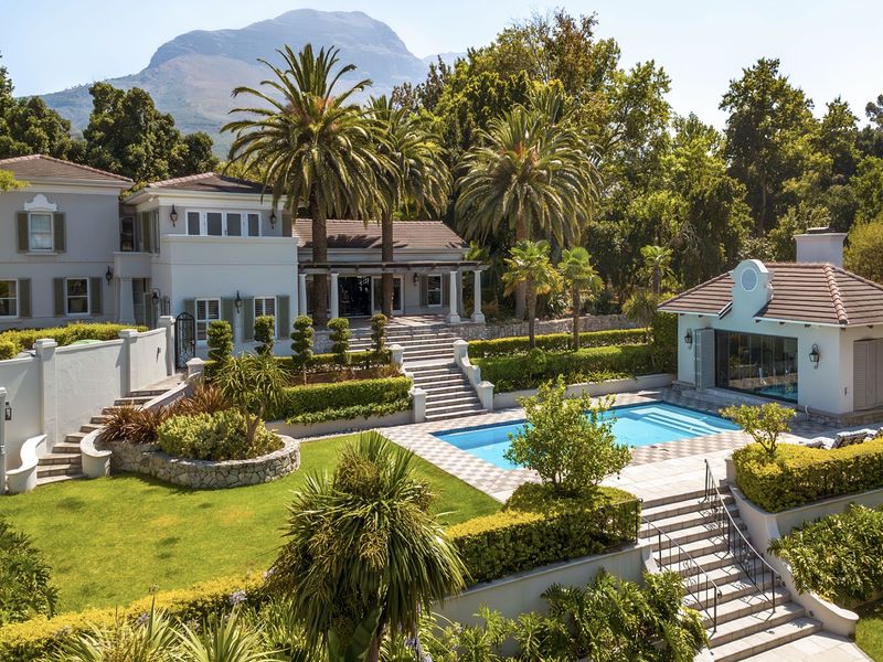 Expansive rear garden featuring a swimming pool, pool house, tiered stone landscaping, and a spacious terrace set against a scenic mountain backdrop.