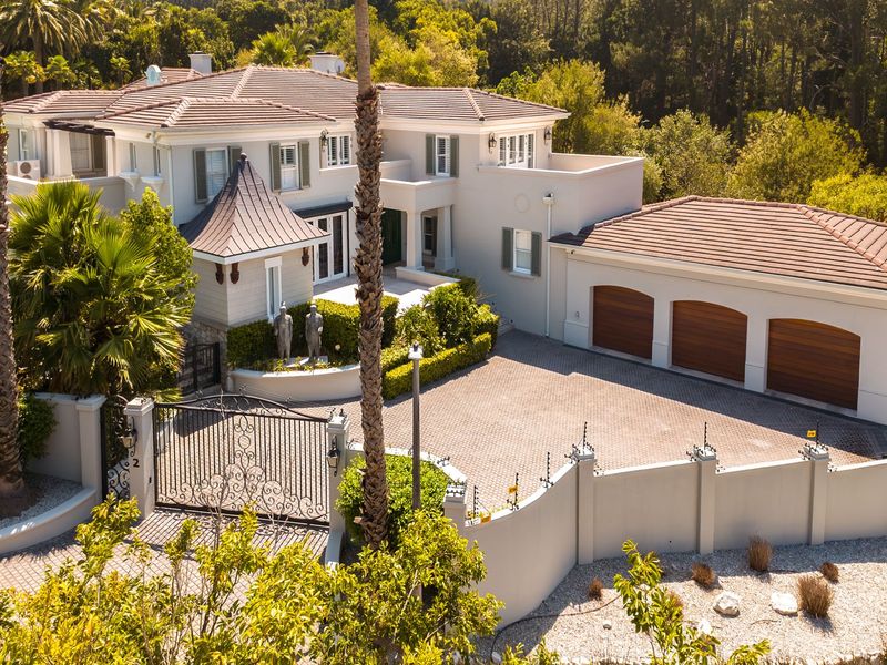 Aerial view of a luxury residence featuring a triple garage, paved driveway, secure gated entrance, and well-maintained perimeter walls with electric fencing.