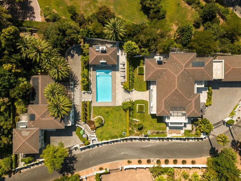 Aerial view of a large residential property featuring a swimming pool, extensive landscaped gardens, multiple roof structures, and a paved driveway.