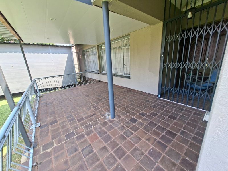 A covered patio area featuring brick paving, a metal security gate, and a protective railing, providing a functional outdoor space.