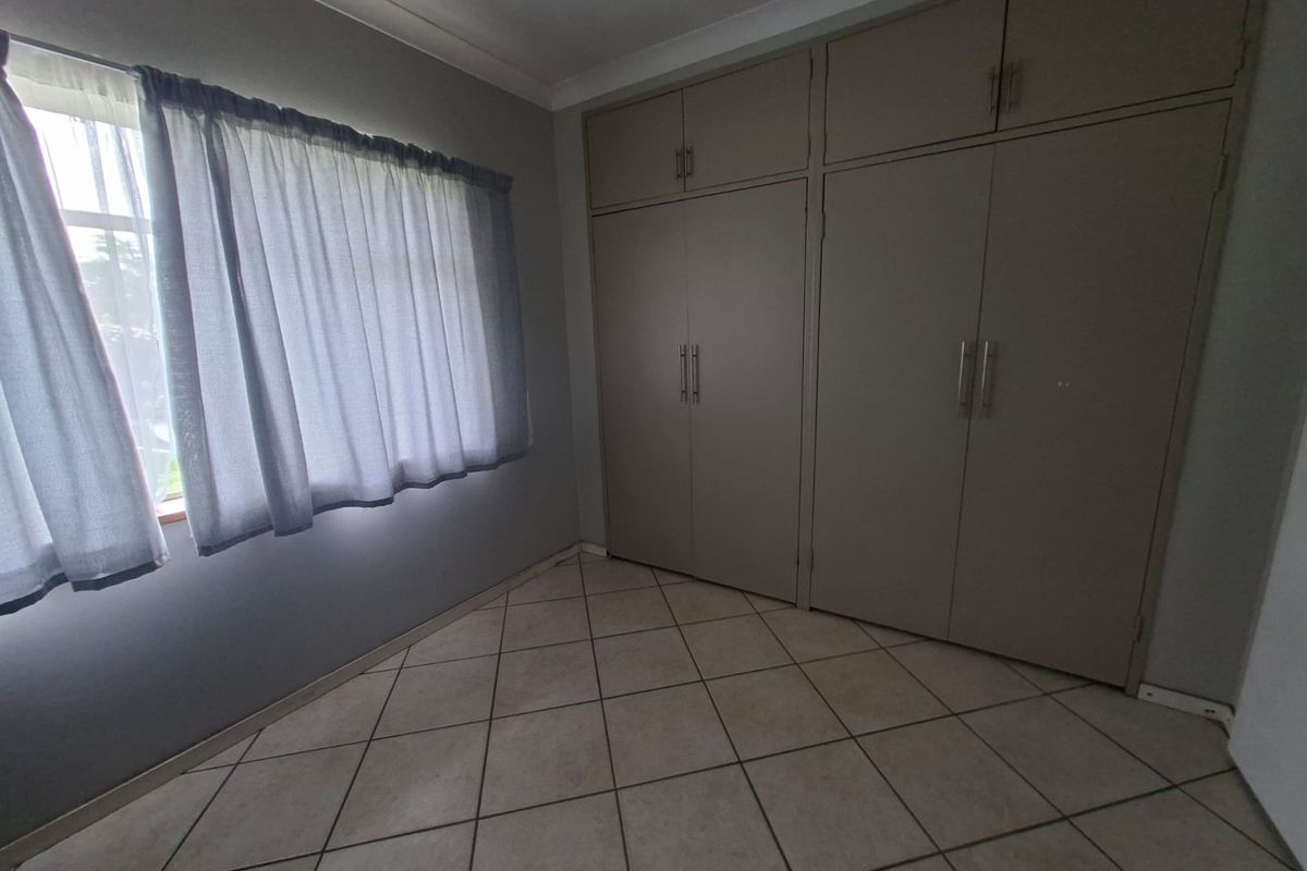 A clean, empty bedroom featuring neutral tiled flooring and ample built-in cupboard storage space.