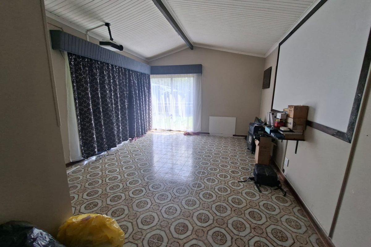 Spacious living area featuring vaulted ceilings, tiled flooring, and sliding glass doors leading to the exterior, currently set up with a projector and screen.