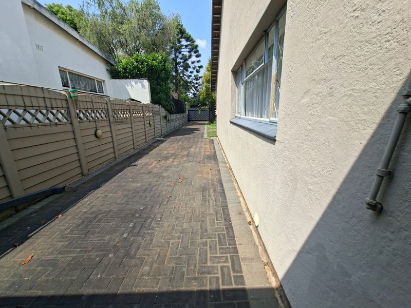 A side passage featuring paved flooring, a precast concrete boundary wall, and exterior wall access along the side of the house.