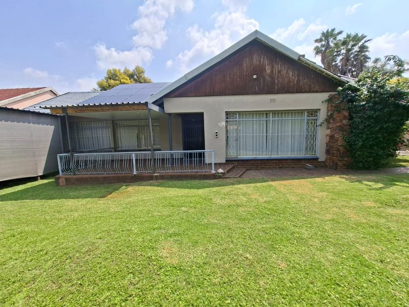 Front elevation of a house featuring a covered patio, solar panels, stone cladding accents, and a well-maintained lawn.