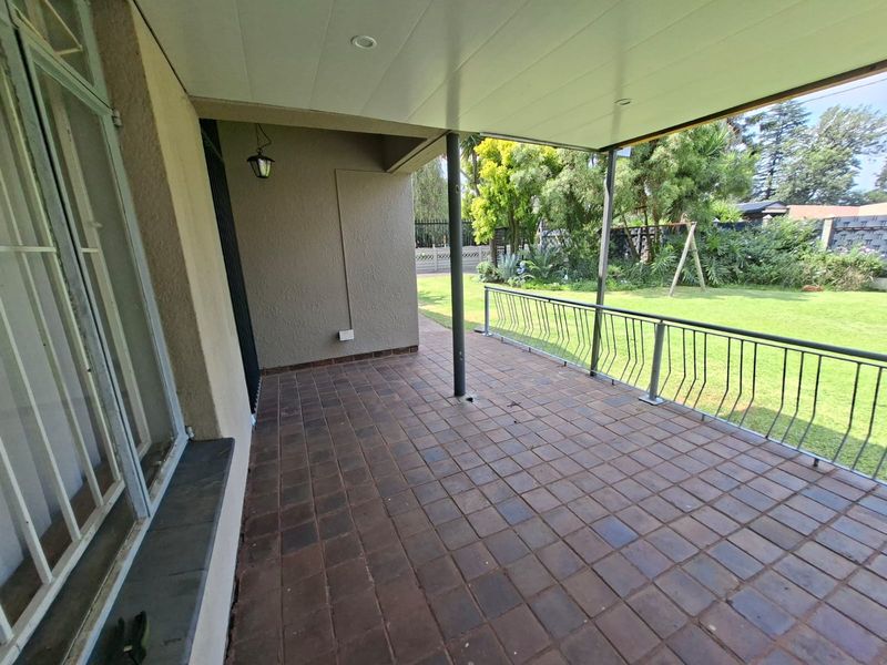 A spacious covered patio featuring tiled flooring, a metal balustrade, and recessed lighting, overlooking a well-maintained garden area.