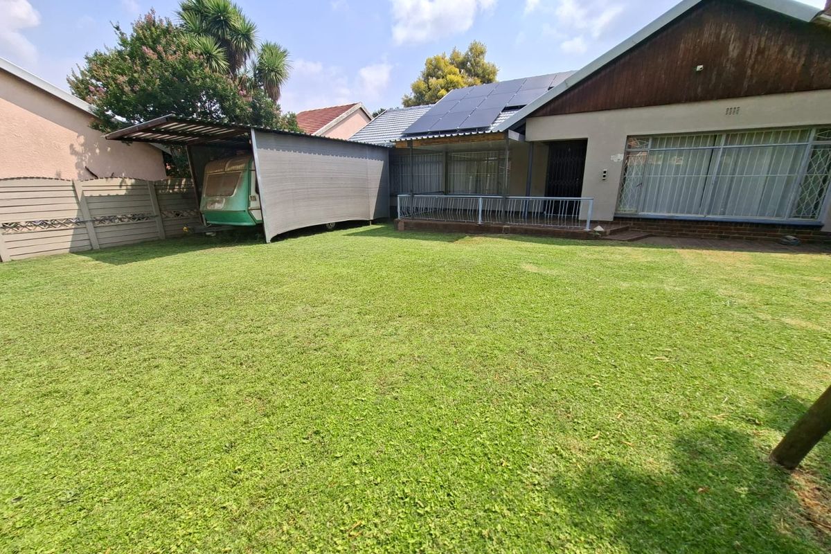 Rear view of the property featuring a spacious lawn, a carport structure, and solar panels installed on the roof.