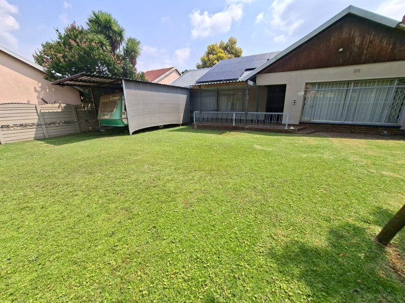 Rear view of the property featuring a spacious lawn, a carport structure, and solar panels installed on the roof.