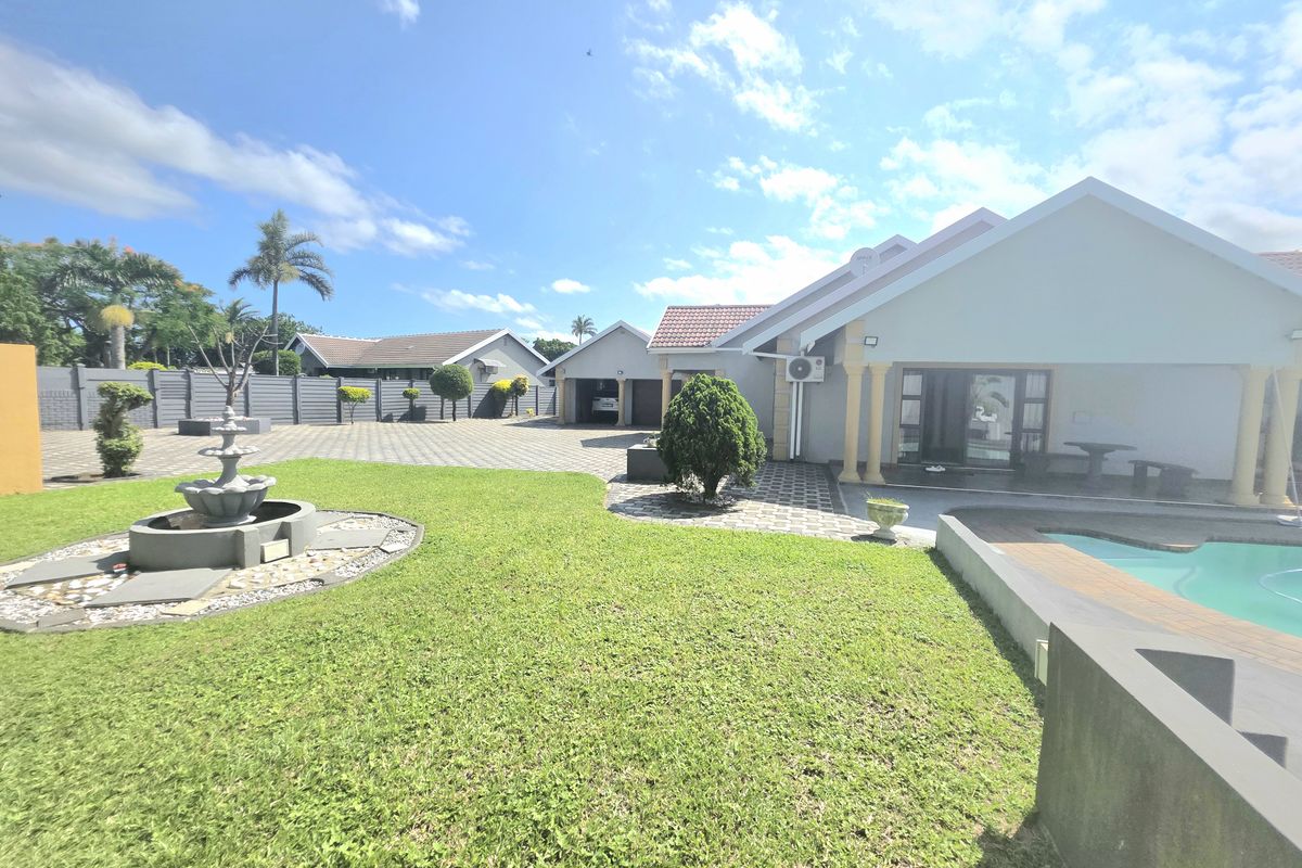 Spacious rear exterior featuring a well-maintained lawn, swimming pool, paved driveway, and a covered patio area.