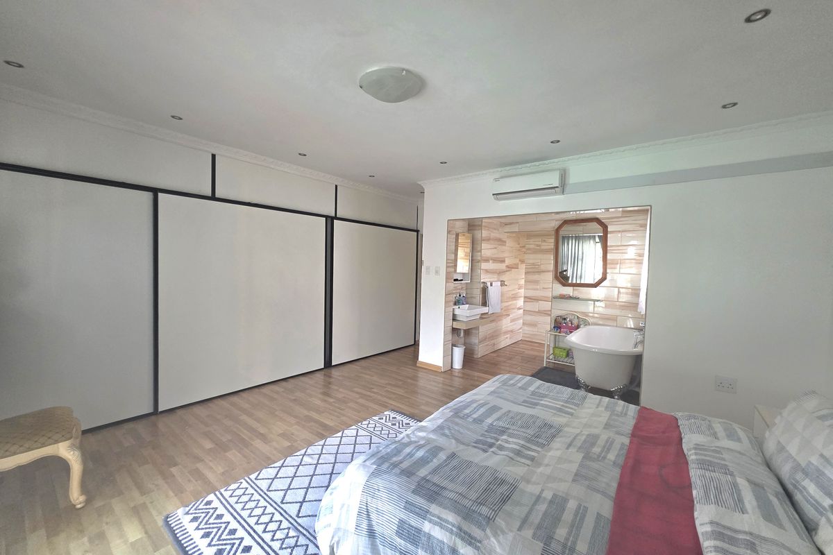 Spacious bedroom featuring extensive built-in cupboards, laminate flooring, and an open-plan ensuite bathroom with a freestanding bathtub and wall-mounted basin.