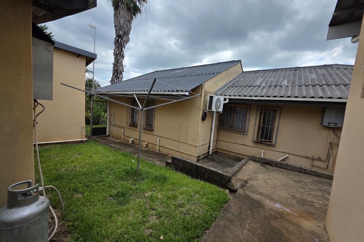 Rear exterior view of the farm property featuring a corrugated metal roof, concrete patio area, and security-barred windows.