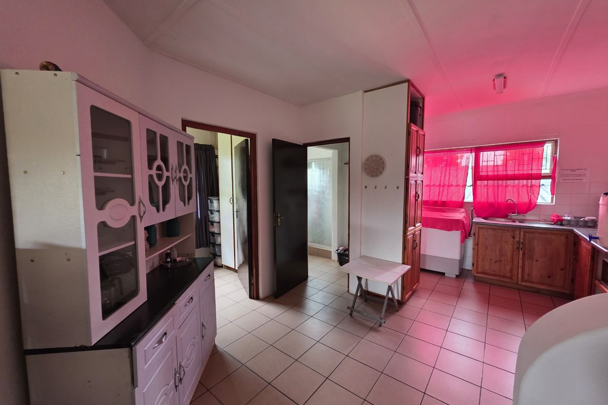 A functional kitchen area featuring tiled flooring, built-in wooden cabinetry, and a stainless steel sink, with direct access to adjacent rooms.