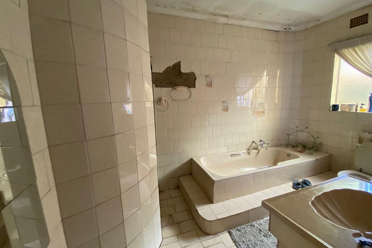 A dated bathroom featuring a built-in bathtub, vanity, and tiled surfaces, currently requiring significant renovation and repair to the walls and ceiling.